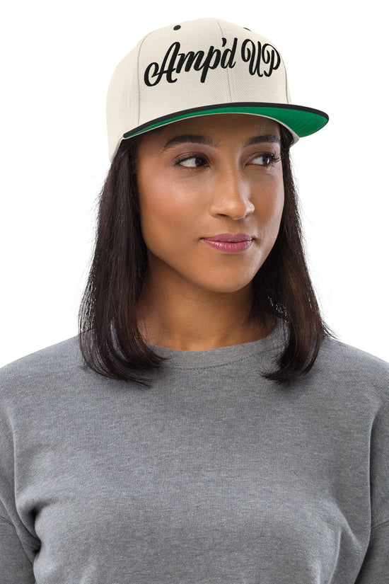 Woman wearing an Amp'd Up cursive 3D Puff Snapback Hat in beige with black lettering