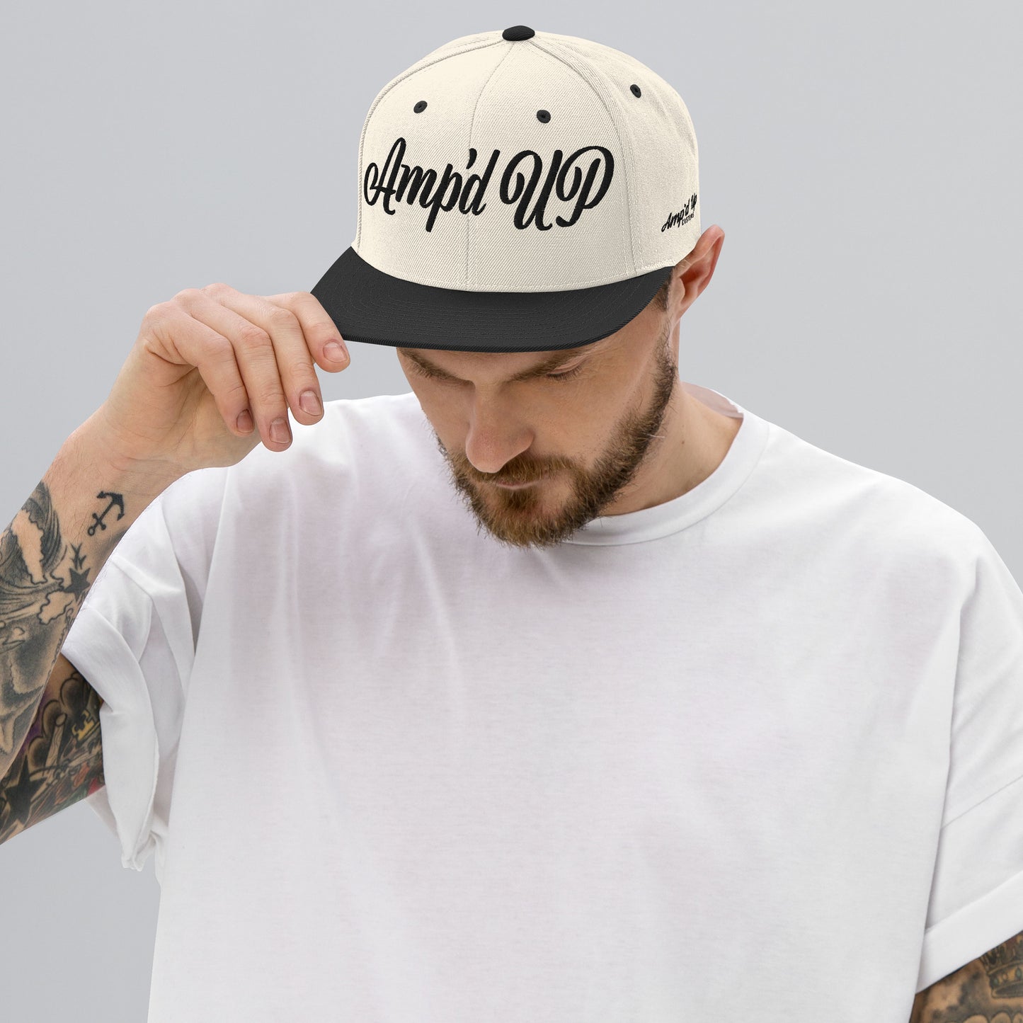 Man wearing Amp'd Up cursive 3D Puff Snapback Hat in cream and black for stylish headwear