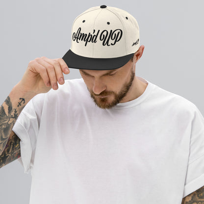 Man wearing Amp'd Up cursive 3D Puff Snapback Hat in cream and black for stylish headwear